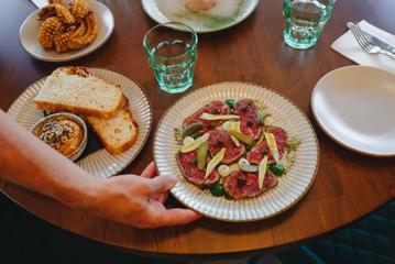 A plate of beef carpaccio and other small sharing plates are set on the table.