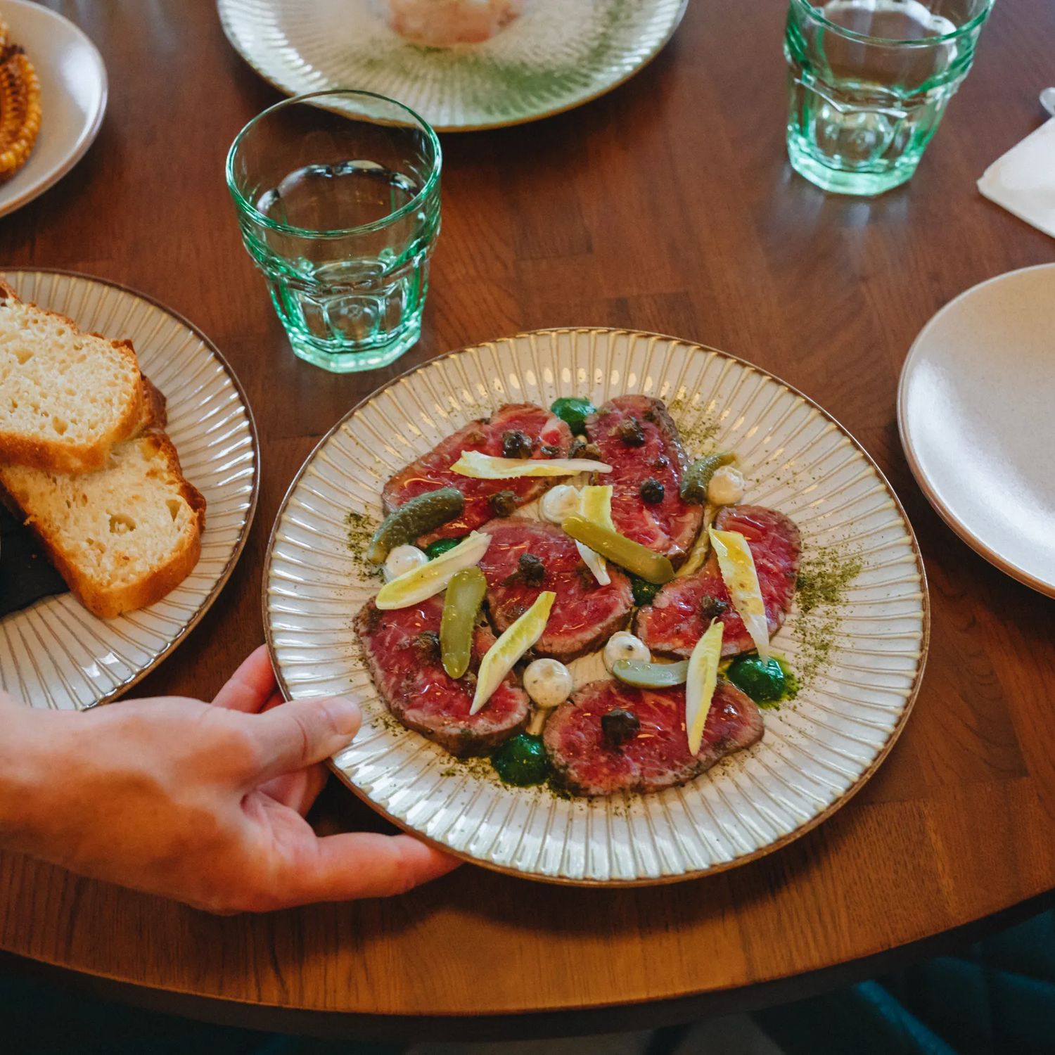 A plate of beef carpaccio and other small sharing plates are set on the table.
