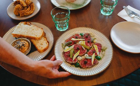 A plate of beef carpaccio and other small sharing plates are set on the table.
