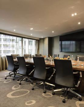 Boardroom table with twelve black leather seats around it. Large television screen on the wall.