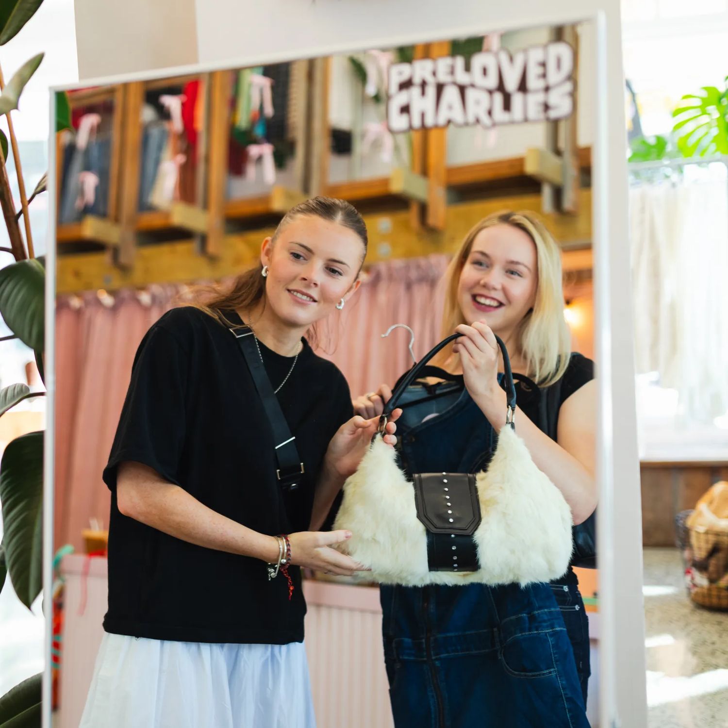 Two people use a mirror inside Preloved Charlies, while clothing is displayed in the store.