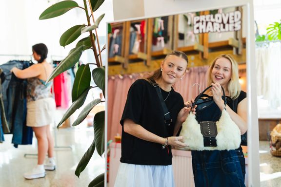 Two people use a mirror inside Preloved Charlies, while clothing is displayed in the store.