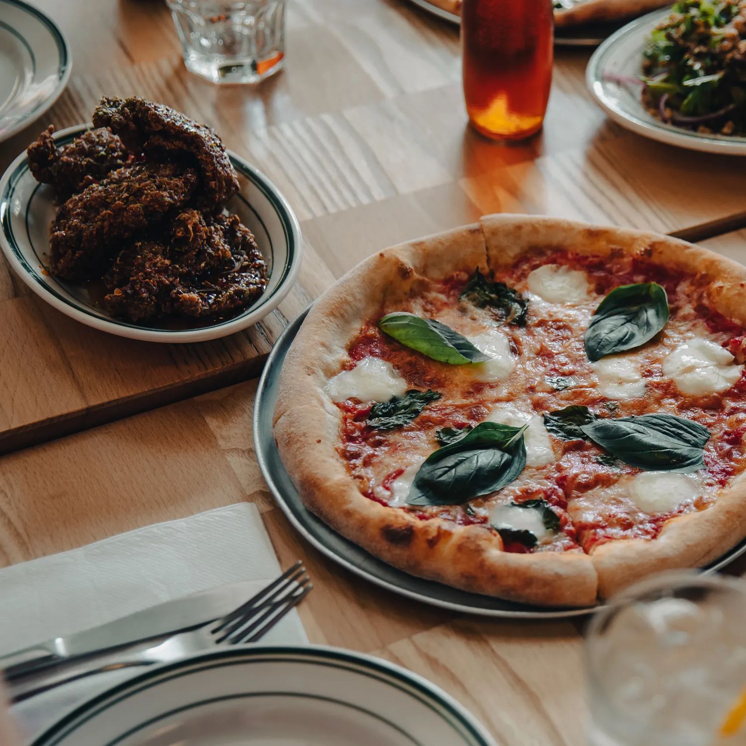 A pizza sits in the middle of a table at Scopa, with glasses, cutlery, and 2 side plates surrounding it.
