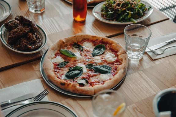 A pizza sits in the middle of a table at Scopa, with glasses, cutlery, and 2 side plates surrounding it.