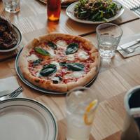 A pizza sits in the middle of a table at Scopa, with glasses, cutlery, and 2 side plates surrounding it.