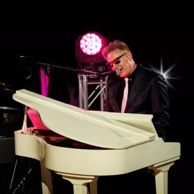 Cam & Same, a New Zealand based tribute band, dressed as Billy Joel and Elton John playing piano and singing on stage.