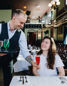 A waiter delivers a cocktail to a smiling patron at Le Bouillon Bel Air, a French restaurant in Wellington.