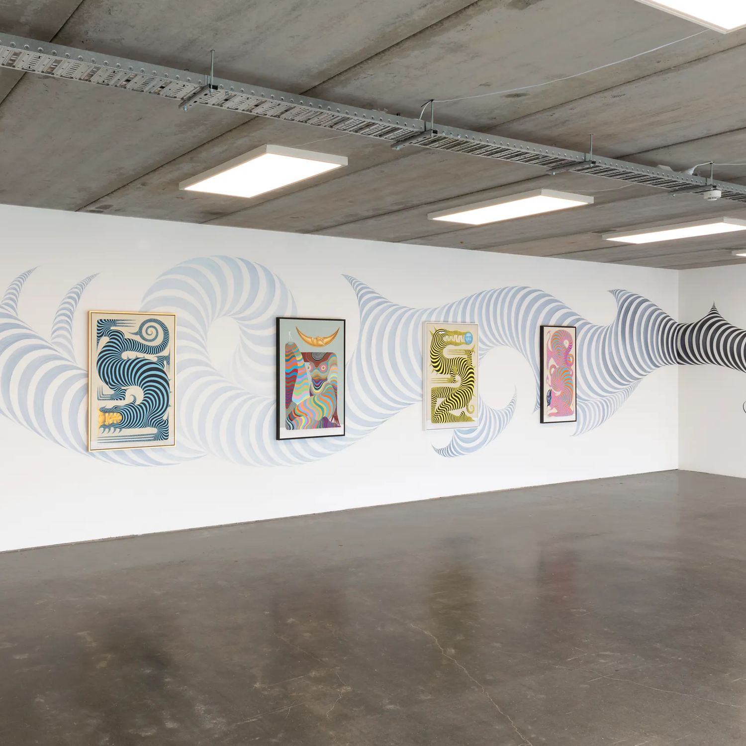 A large room wth white walls, a concrete floor and an exposed ceiling with a collection of contemporary prints on display.