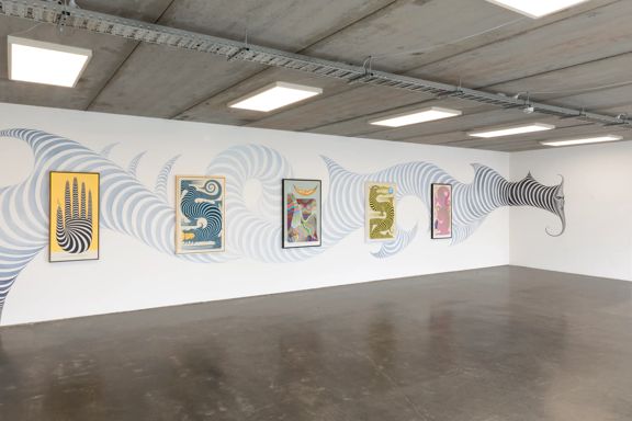 A large room wth white walls, a concrete floor and an exposed ceiling with a collection of contemporary prints on display.