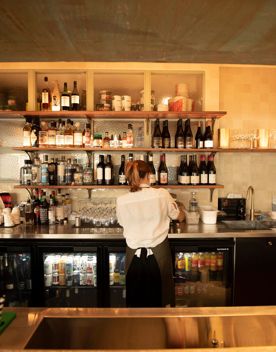 Wait staff standing at a kitchen bench facing a wall lined with liquor bottles and wine bottles.