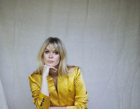 Dolly Alderton crouches in front of a white backdrop wearing a vibrant, shiny, yellow suit.