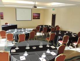 Inside the Jerningham room at Copthorne hotel, 4 circle tables each with 5 chairs all face a projector at the front of the room.