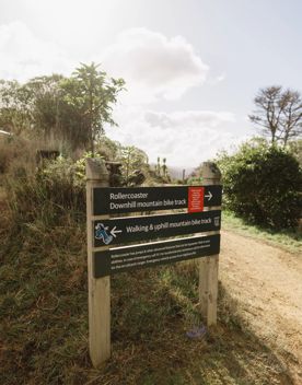 Wooden directional signpost showing Roller Coaster downhill mountain bike track to the right, and the walking and uphill mountainbike track to the left.