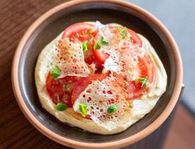 Five slices of heirloom tomato arranged in a circle placed on top of a saffron aioli topped with fresh herbs on a small dark grey place.