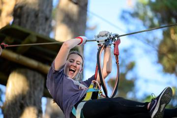 Close-up of a teenager with a big smile on their face as they slide down a wire in amongst the trees at Adrenalin Forest.