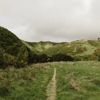 A narrow path along a grassy hillside under a cloudy sky.