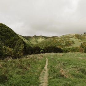A narrow path along a grassy hillside under a cloudy sky.