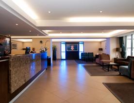 The lobby at the Copthorne Hotel has a cream-tiled floor with a marble check-in desk. Brown rugs and chairs make up the lobby.