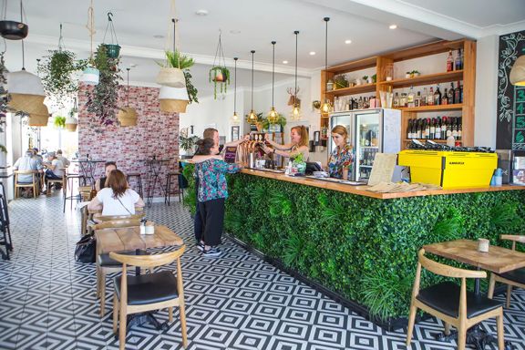 Inside The Botanist, a restaurant in Lyall Bay, Wellington. The floor has black and white tiles, potted plants hanging from the ceiling and a few patrons enjoying food.