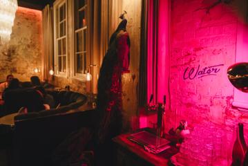 Inside Wellington’s Puffin Wine Bar. It has exposed brick walls illuminated by bright pink light, a taxidermied peacock, and round booth seating.