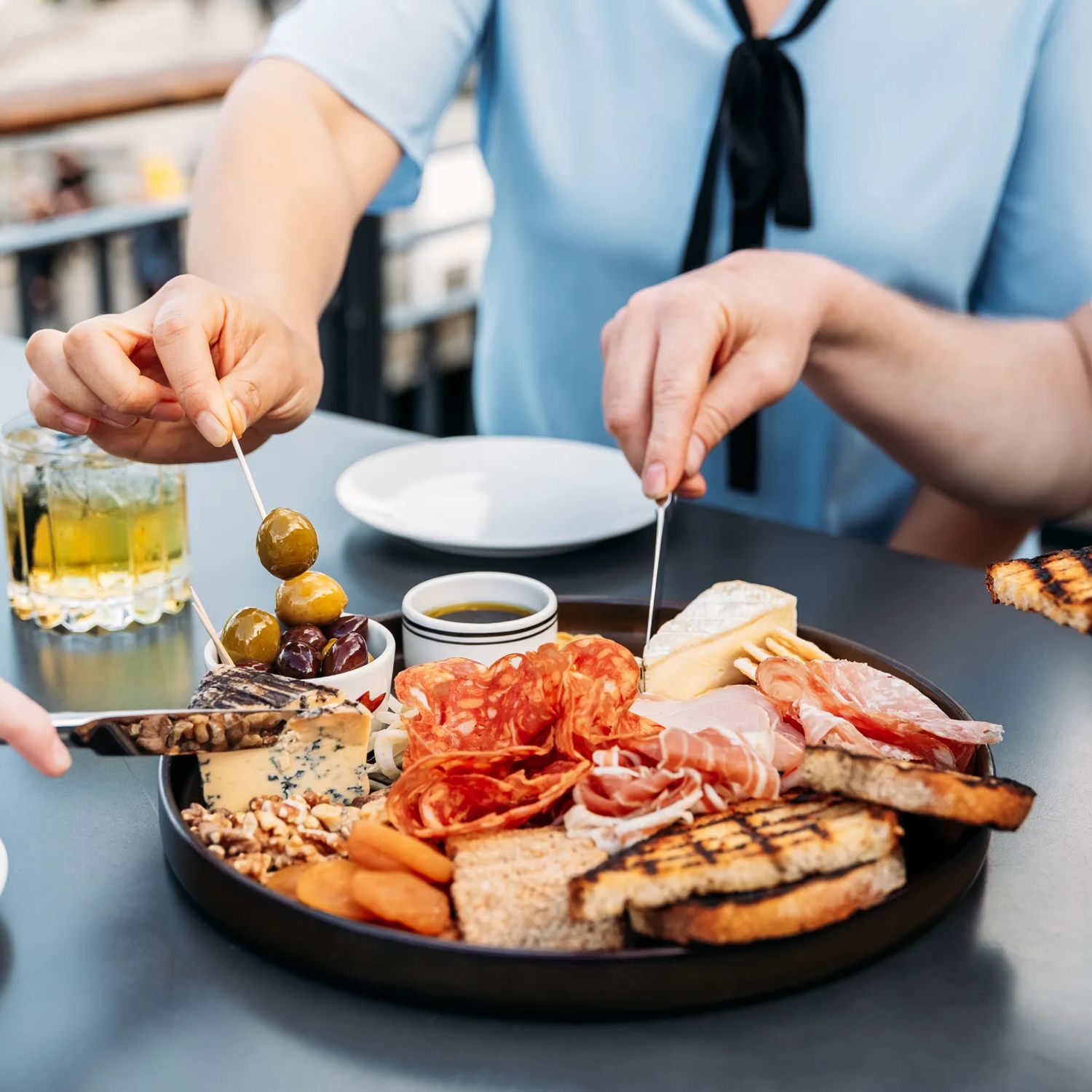Three people grabbing food from a charcuterie board at Foxglove on Queens Wharf.