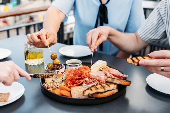 Three people grabbing food from a charcuterie board at Foxglove on Queens Wharf.