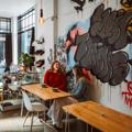 Two friends enjoy coffee in a sunny café with graffitied walls.