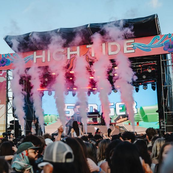 High Tide festival stage with pink illustrations surrounding it, and special effects smoke.