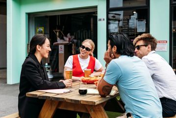 Four people sitting outside on a picnic table at Heyday Beer Co enjoying pints of beer.