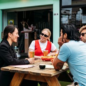 Four people sitting outside on a picnic table at Heyday Beer Co enjoying pints of beer.