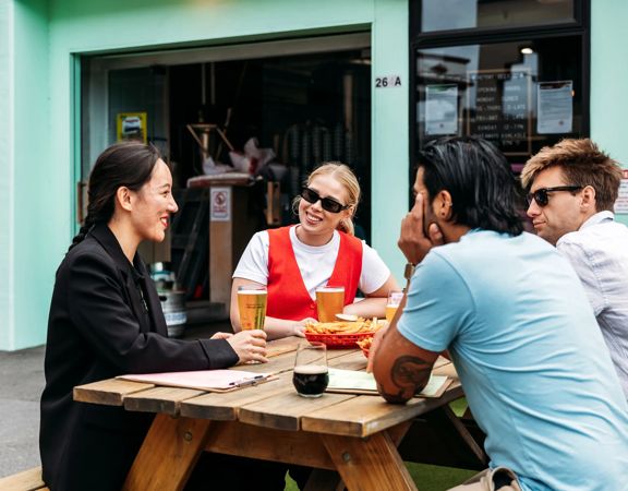 Four people sitting outside on a picnic table at Heyday Beer Co enjoying pints of beer.