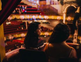 Two people sitting in the St James Theatre watching a show with red and gold in the background.
