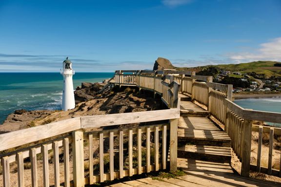 Wooden walkway leading to the Castlepoint lighthouse with hills in background and blue ocean.
