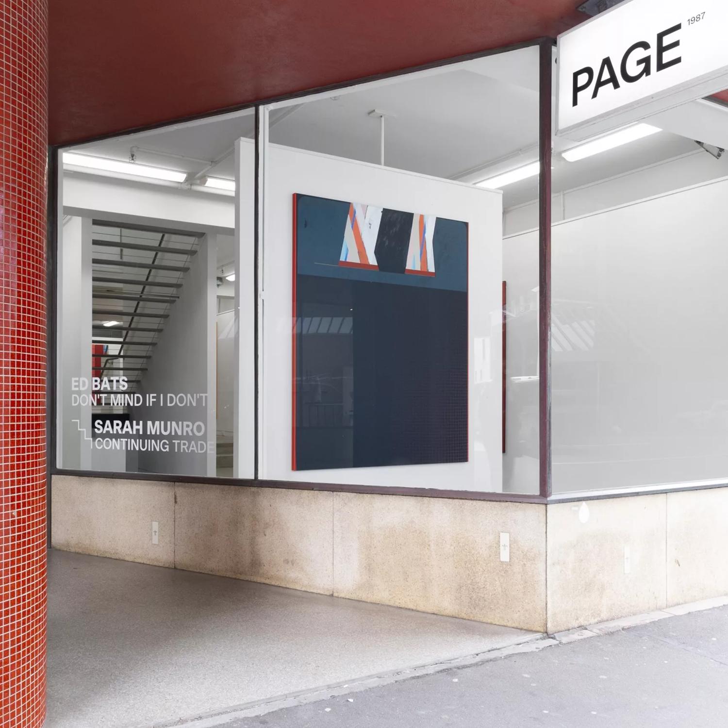 View of the outside of the Page Galleries  building from the footpath. A thick round red tiled pillar is to the left of the image. The front window of the gallery is sparse apart from one large painting. 