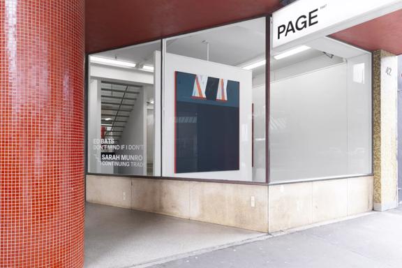 View of the outside of the Page Galleries  building from the footpath. A thick round red tiled pillar is to the left of the image. The front window of the gallery is sparse apart from one large painting.