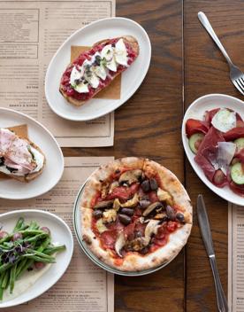 Looking down at various dishes served at Ombra on the wooden table, including pizzas, salads and Toast.