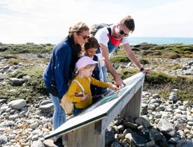 A family of four is looking at an information plaque on Kapiti Island.