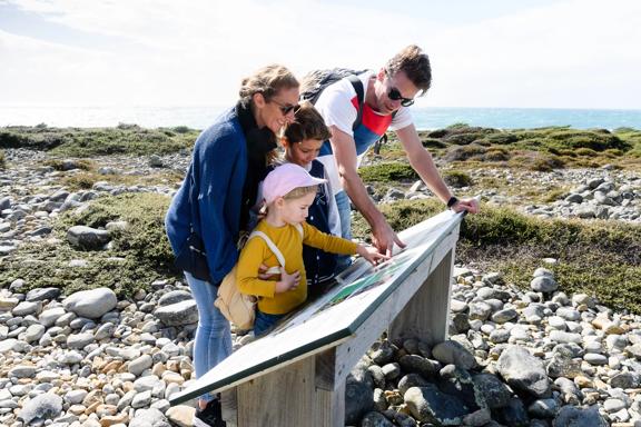 A family of four is looking at an information plaque on Kapiti Island.