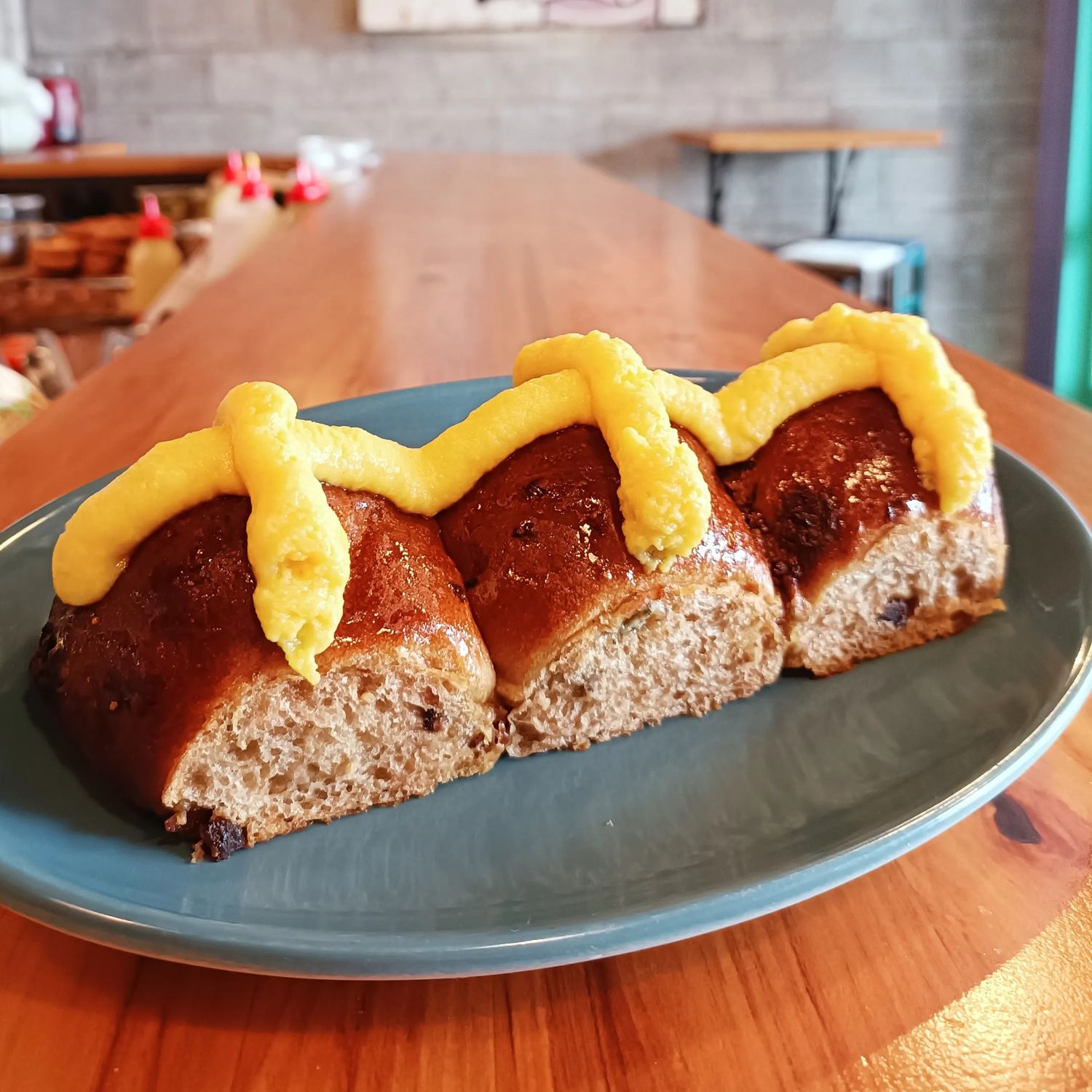 Three hot cross buns topped with thick yellow custard crosses on a blue plate.