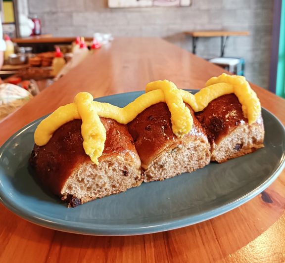 Three hot cross buns topped with thick yellow custard crosses on a blue plate.