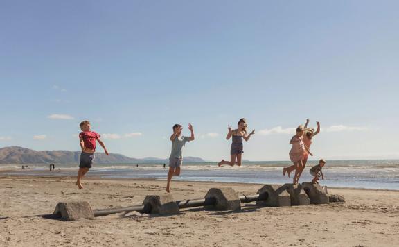 Six children jump off cement blocks on a sandy beach.