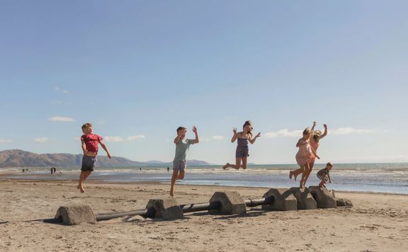 Six children jump off cement blocks on a sandy beach.