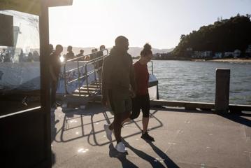 Two people holding hands walking together on a concrete dock with a small ferry boat where other passengers are disembarking behind them.