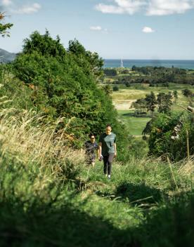 Two people hike up a grassy hill on Te Au Track at Hemi Matenga Scenic Reserve.