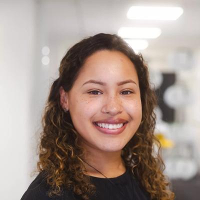 A head and shoulders shot of Madelaine Narvaez, the Business Events Wellington administrator. She has curly, shoulder-length brown hair and wears a black long-sleeve top.