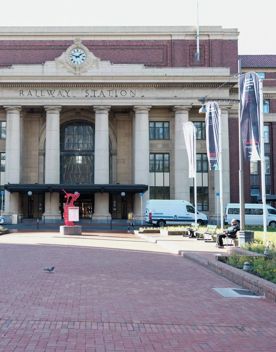 The Wellington Railway Station building is a red brick building with stone columns. A path leads up the middle, with gardens on either side.