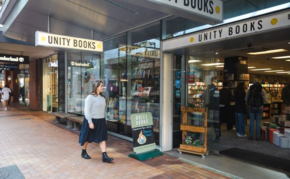 A person reads a book inside Unity books, while standing in front of a colourful bookshelf.