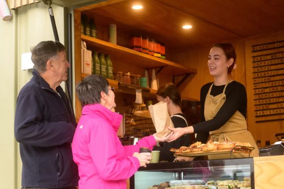 A barista hands a brown paper bag with food in it to a customer at Little Green Olive in Porirua.