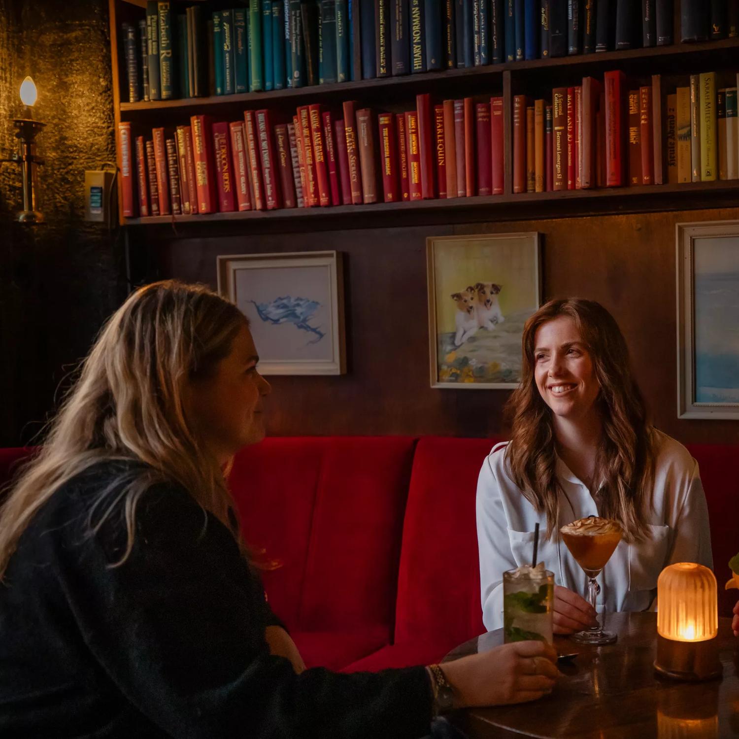 Three people sit at a table enjoying drinks at The Library, a cocktail bar in Te Aro, Wellington.