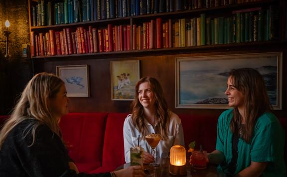 Three people sit at a table enjoying drinks at The Library, a cocktail bar in Te Aro, Wellington.